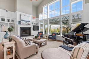 Living area with ceiling fan, a high ceiling, wood finished floors, and a fireplace with raised hearth