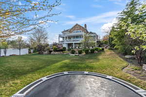 Back of house with a lawn, fence, a chimney, and a balcony