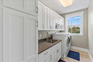 Clothes washing area with washer and clothes dryer, a sink, light tile patterned flooring, baseboards, and cabinet space