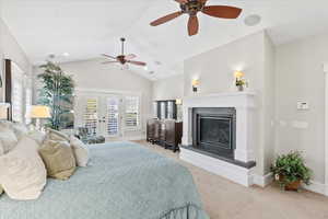 Bedroom with french doors, access to exterior, vaulted ceiling, a glass covered fireplace, and light colored carpet