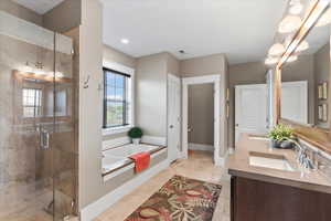 Bathroom featuring a bath, a sink, double vanity, a stall shower, and baseboards