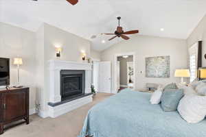 Bedroom with light carpet, vaulted ceiling, a glass covered fireplace, baseboards, and a ceiling fan