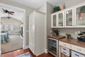 Bar featuring dark wood finished floors, vaulted ceiling, baseboards, a ceiling fan, and beverage cooler
