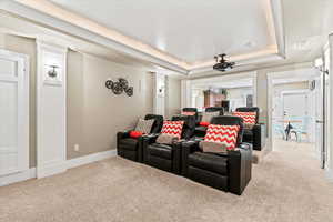 Carpeted cinema with a tray ceiling, visible vents, and baseboards