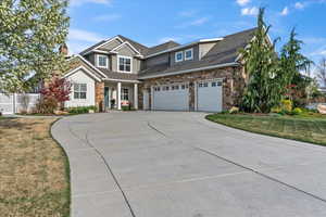 View of front of house with a chimney, driveway, stone siding, fence, and a garage