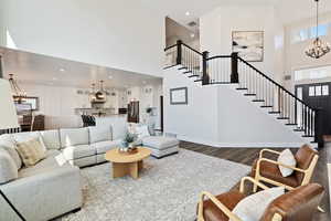 Living area featuring dark wood finished floors, a towering ceiling, stairs, and an inviting chandelier