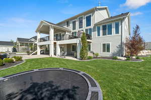 Back of property with a trampoline, a lawn, stairs, a balcony, and a patio