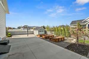 View of patio / terrace featuring a vegetable garden, a fenced backyard, a residential view, an outbuilding, and a storage unit