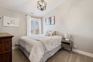 Carpeted bedroom with lofted ceiling, baseboards, visible vents, and an inviting chandelier