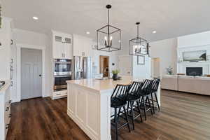 Kitchen with a sink, a breakfast bar, white cabinets, appliances with stainless steel finishes, and dark wood-type flooring