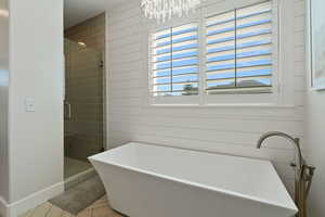 Bathroom with baseboards, a soaking tub, an inviting chandelier, and a stall shower