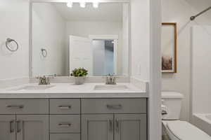 Bathroom with double vanity, toilet, shower / bathtub combination, and a sink