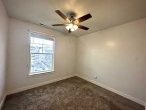 Empty room featuring a ceiling fan, visible vents, dark carpet, and baseboards