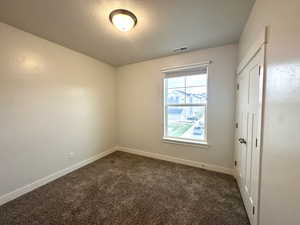 Empty room featuring a textured ceiling, visible vents, dark carpet, and baseboards