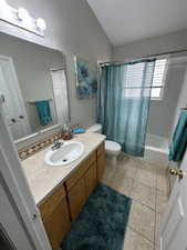 Bathroom with lofted ceiling, tile patterned floors, toilet, vanity, and shower / tub combo with curtain