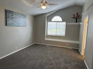 Empty room featuring dark colored carpet, vaulted ceiling, visible vents, baseboards, and a ceiling fan