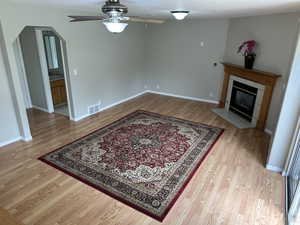 Living area with ceiling fan, a tile fireplace, visible vents, and light wood-style flooring