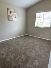 Empty room with vaulted ceiling, visible vents, carpet flooring, and baseboards
