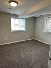 Spare room featuring baseboards, a healthy amount of sunlight, dark colored carpet, and a textured ceiling