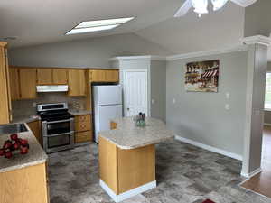 Kitchen featuring under cabinet range hood, freestanding refrigerator, a center island, range with two ovens, and vaulted ceiling with skylight