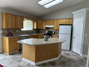 Kitchen with stainless steel appliances, a sink, tasteful backsplash, vaulted ceiling, and under cabinet range hood