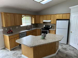 Kitchen featuring stainless steel range with electric cooktop, under cabinet range hood, vaulted ceiling, a sink, and freestanding refrigerator
