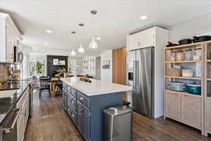 Kitchen featuring stainless steel appliances, a center island, white cabinetry, and hanging light fixtures
