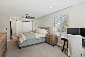 Bedroom featuring light colored carpet, a barn door, and multiple windows