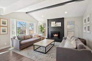 Living room featuring vaulted ceiling with beams, baseboards, recessed lighting, wood finished floors, and a brick fireplace