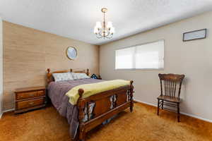 Carpeted bedroom featuring a textured ceiling, baseboards, and an inviting chandelier