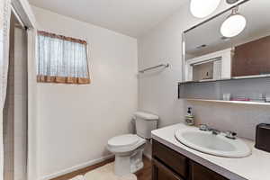 Full bath with a tile shower, visible vents, toilet, vanity, and baseboards