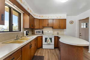Kitchen featuring white range with electric stovetop, a sink, light countertops, stainless steel microwave, and a peninsula