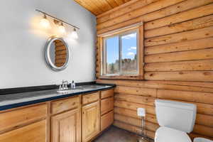 Bathroom featuring wooden ceiling, toilet, log walls, and vanity