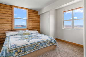 Bedroom with carpet, log walls, baseboards, and multiple windows