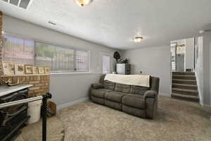 Carpeted living area with a textured ceiling, baseboards, stairs, and visible vents