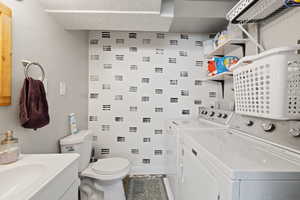 Bathroom with a sink, baseboards, washing machine and dryer, toilet, and tile patterned flooring