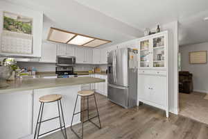 Kitchen with a sink, light wood-style flooring, white cabinets, a peninsula, and appliances with stainless steel finishes