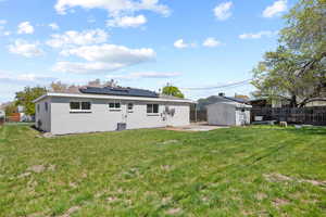 Rear view of house with a patio area, a lawn, a fenced backyard, solar panels, and a storage unit