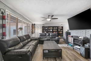 Living room with wood finished floors, a textured ceiling, crown molding, and a ceiling fan
