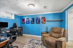 Office with a textured ceiling, visible vents, baseboards, wood finished floors, and ornamental molding