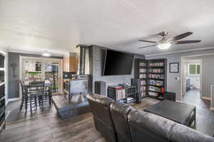 Living area featuring ceiling fan, dark wood-style flooring, a wood stove, and a textured ceiling