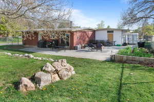Rear view of house featuring fence, a lawn, brick siding, and a patio