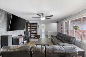 Living room with wood finished floors, crown molding, baseboards, a textured ceiling, and ceiling fan