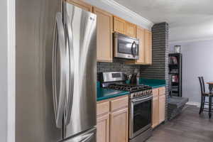 Kitchen featuring light brown cabinetry, stainless steel appliances, ornamental molding, decorative backsplash, and a textured ceiling