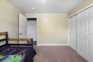 Carpeted bedroom with baseboards, a textured ceiling, and a closet