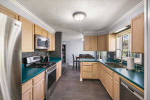 Kitchen with light brown cabinets, ornamental molding, a sink, a textured ceiling, and appliances with stainless steel finishes