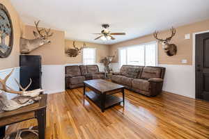 Living room with light wood-style floors, a wainscoted wall, and a ceiling fan