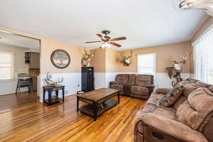 Living room with light wood-style flooring, a wealth of natural light, a ceiling fan, and wainscoting