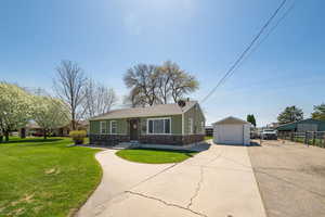 View of front of home featuring a detached garage, concrete driveway, a front lawn, fence, and an outbuilding