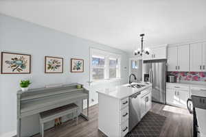 Kitchen with a sink, a kitchen island with sink, stainless steel appliances, a notable chandelier, and dark wood-style floors